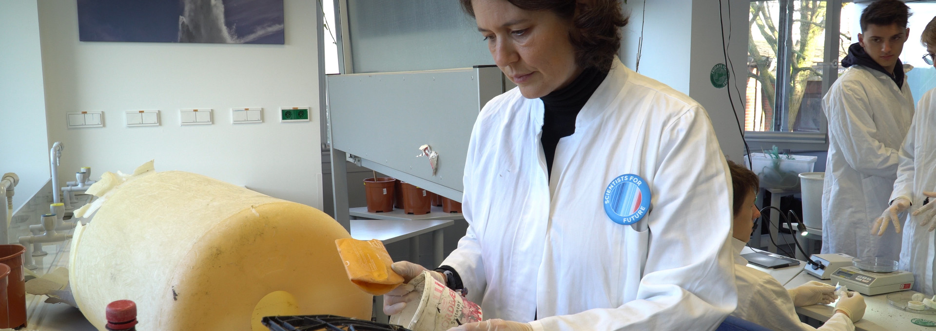 Scientist in white lab coat with a big yellow bucket turned marine litter