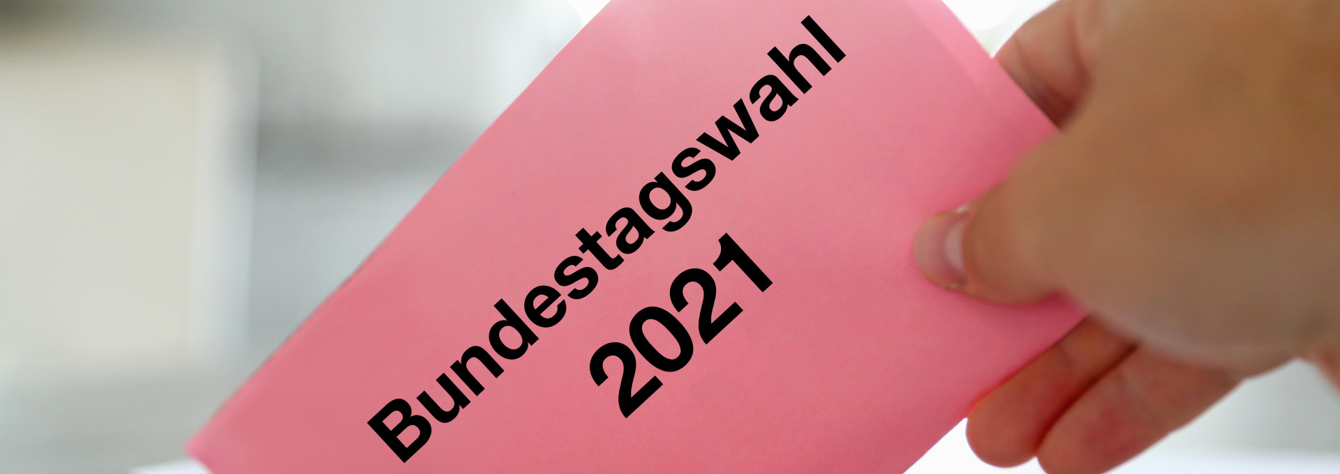 Hand wirft Umschlag mit Aufschrift "Bundestagswahl 2021" in Wahlurne