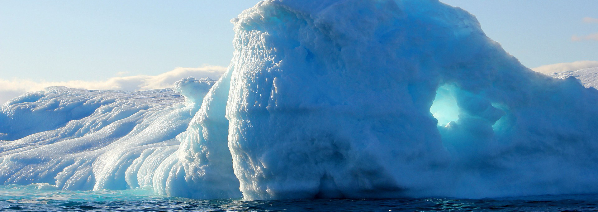 A blue and white iceberg rises out of the water at an icy landscape