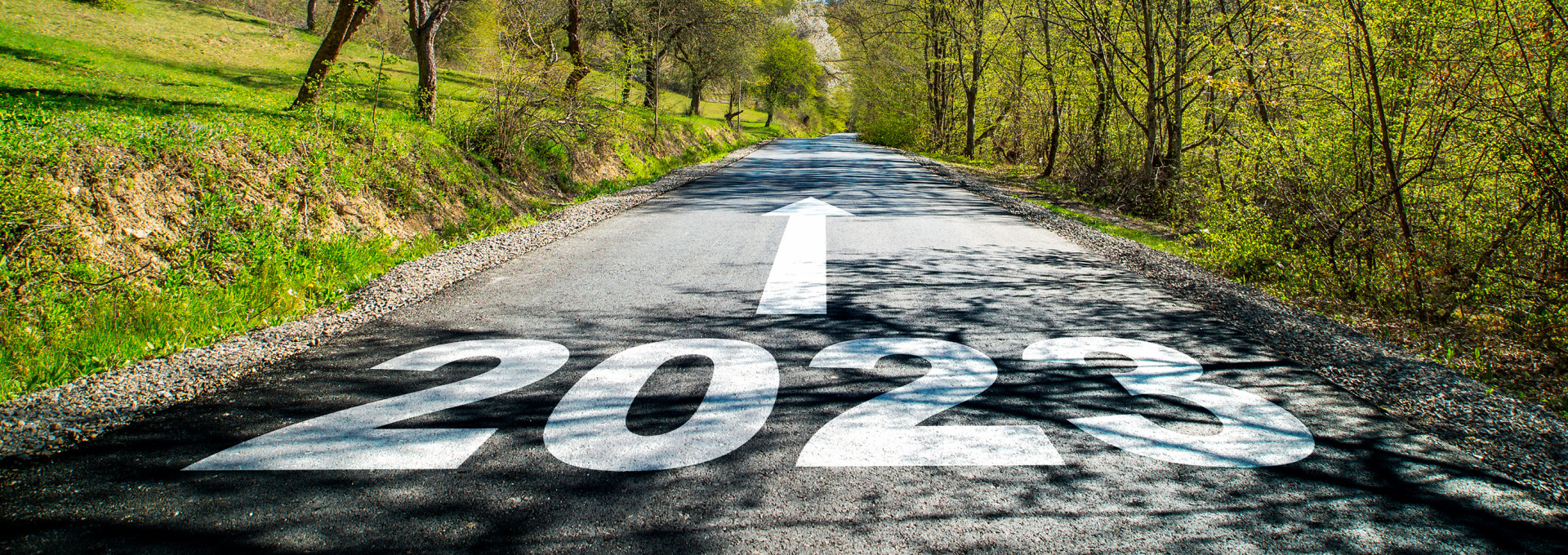 Eine Straße durch grüne Landschaft, auf der Fahrbahn steht groß "2023" - ein Pfeil zeigt darüber geradeaus die Straße hinauf.