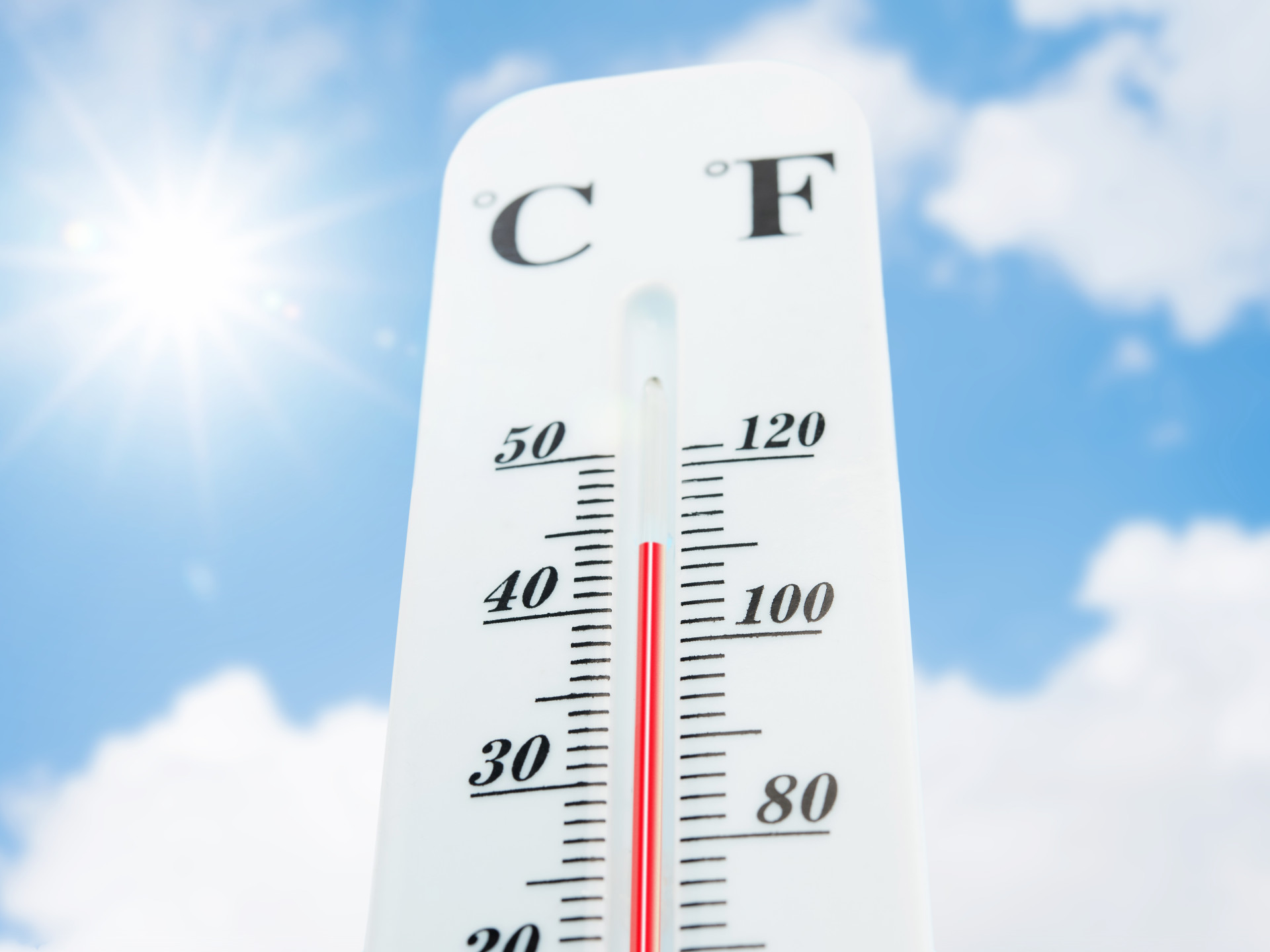 Ein Thermometer zeigt eine hohe Temperatur über 44 Grad an. Sonne und Himmel sind im Hintergrund zu sehen.