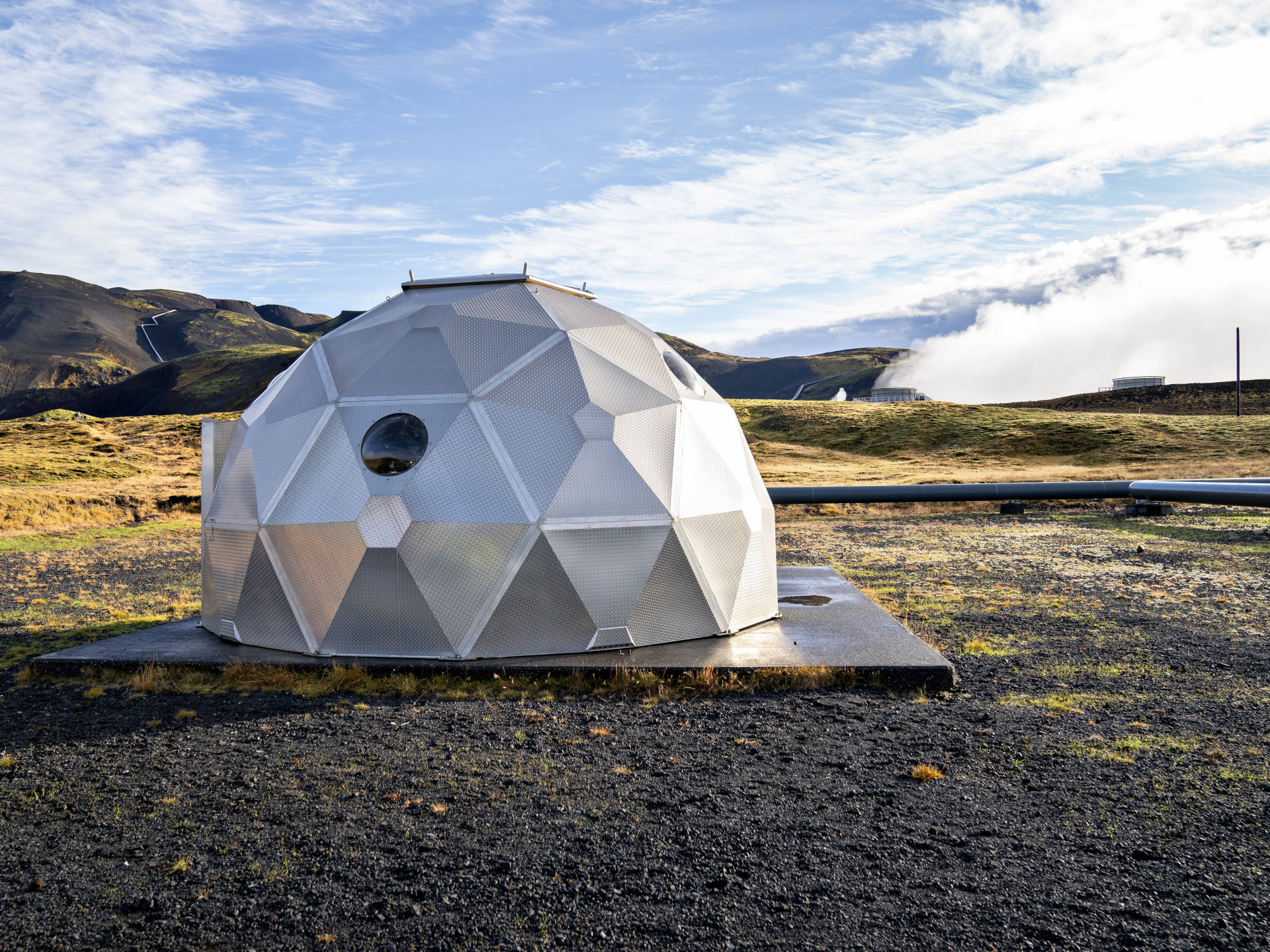 Silbernes Iglu in karger Landschaft, mit Dampf im Hintergrund