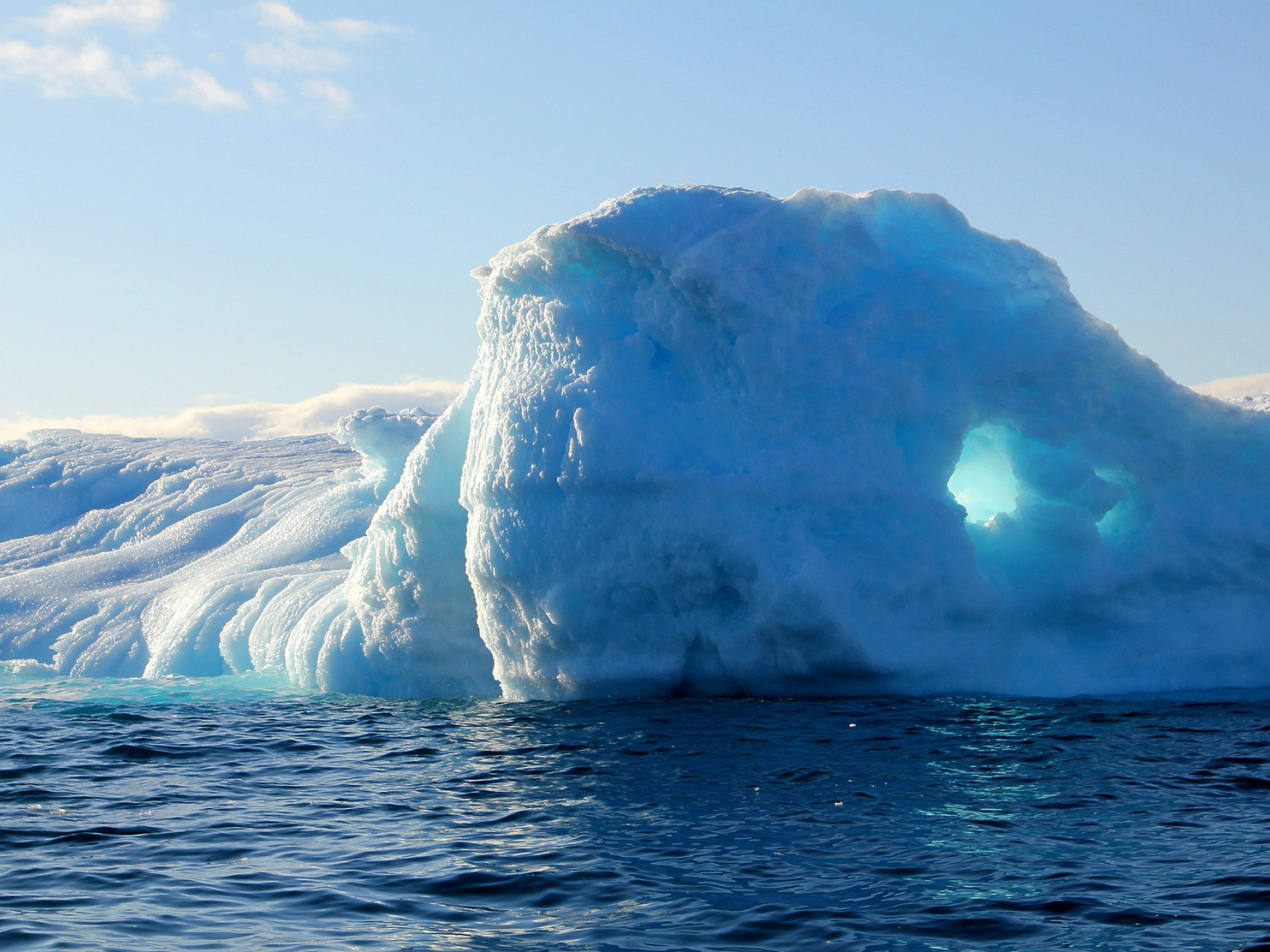 A blue and white iceberg rises out of the water at an icy landscape