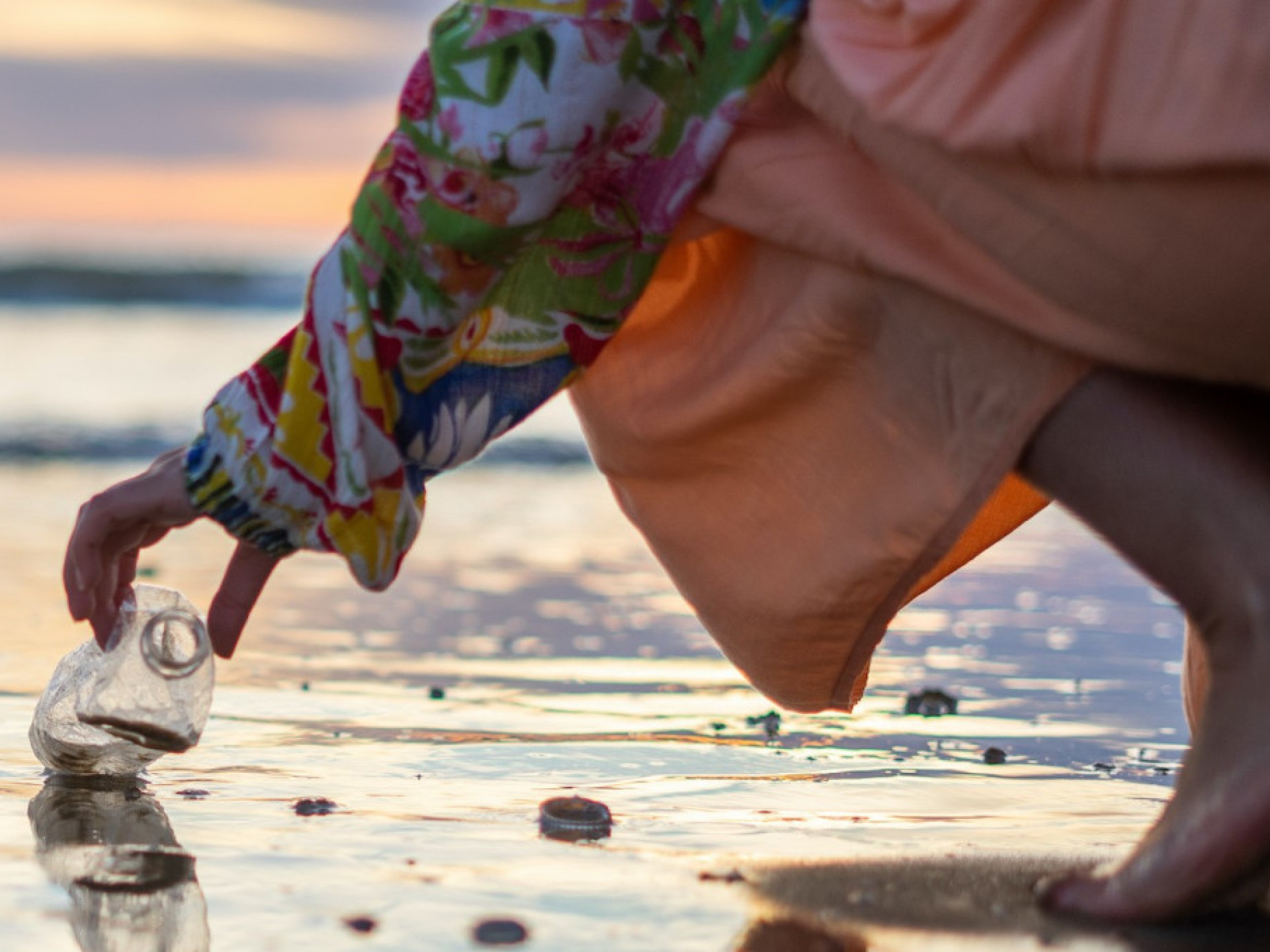 Eine Person hebt eine Plastikflasche von einem Strand auf