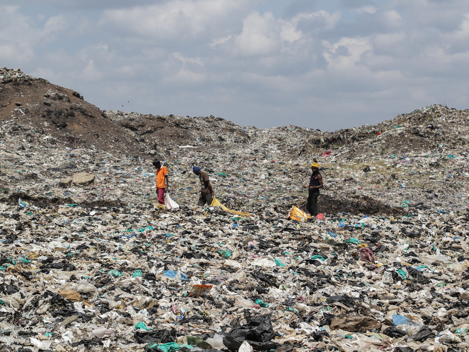 Drei Personen laufen über eine riesige Müllhalde mit Plastik und anderem Müll