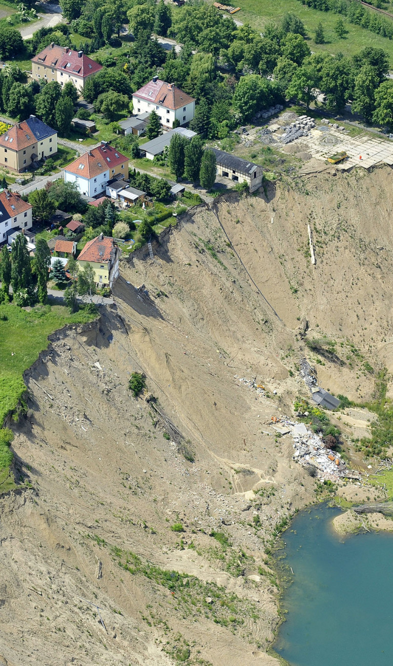 Häuser an einem Hang ohne Vegetation, der zu einem kleinen See herunterführt.