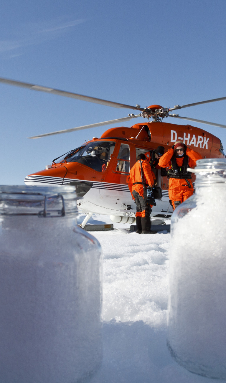 Einweckgläser mit Schneeproben vor rotem Hubschrauber in der Arktis