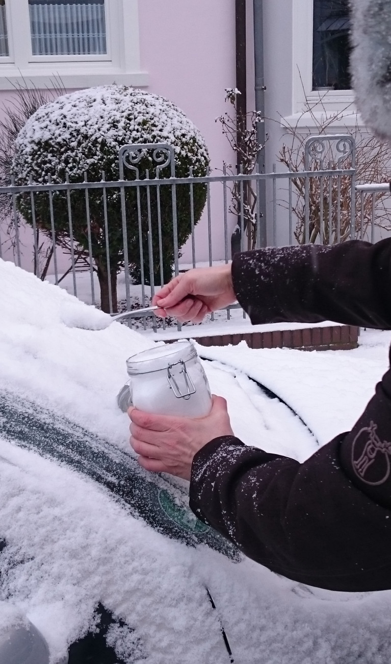 Wissenschaftlerin in Winterjacke sammelt Schneeprobe von einem Auto