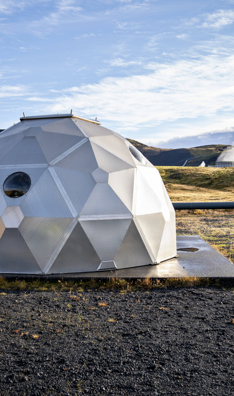 Silbernes Iglu in karger Landschaft, mit Dampf im Hintergrund