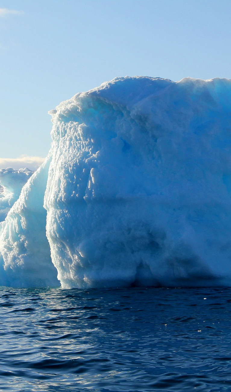 Ein blau-weißer Eisberg ragt an einer Eislandschaft aus dem Wasser