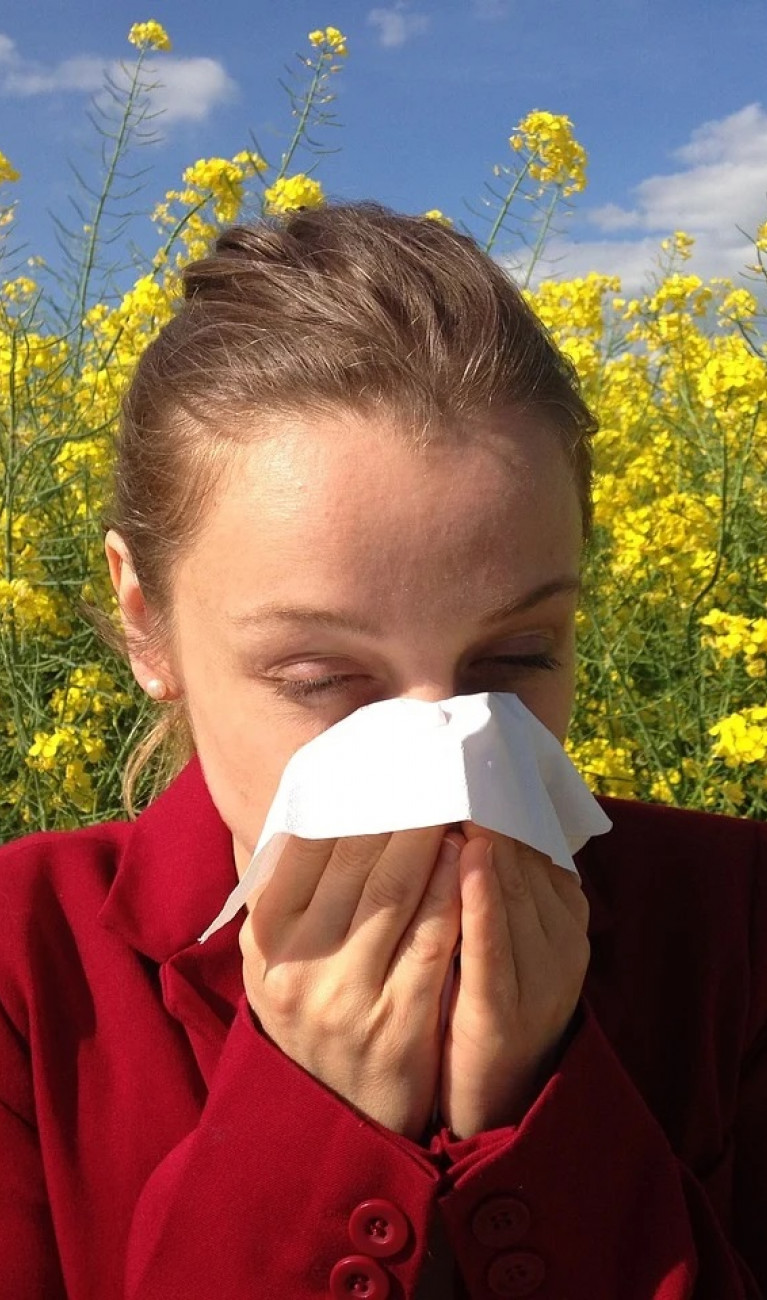 Woman blowing her nose in front of a field of rapeseed