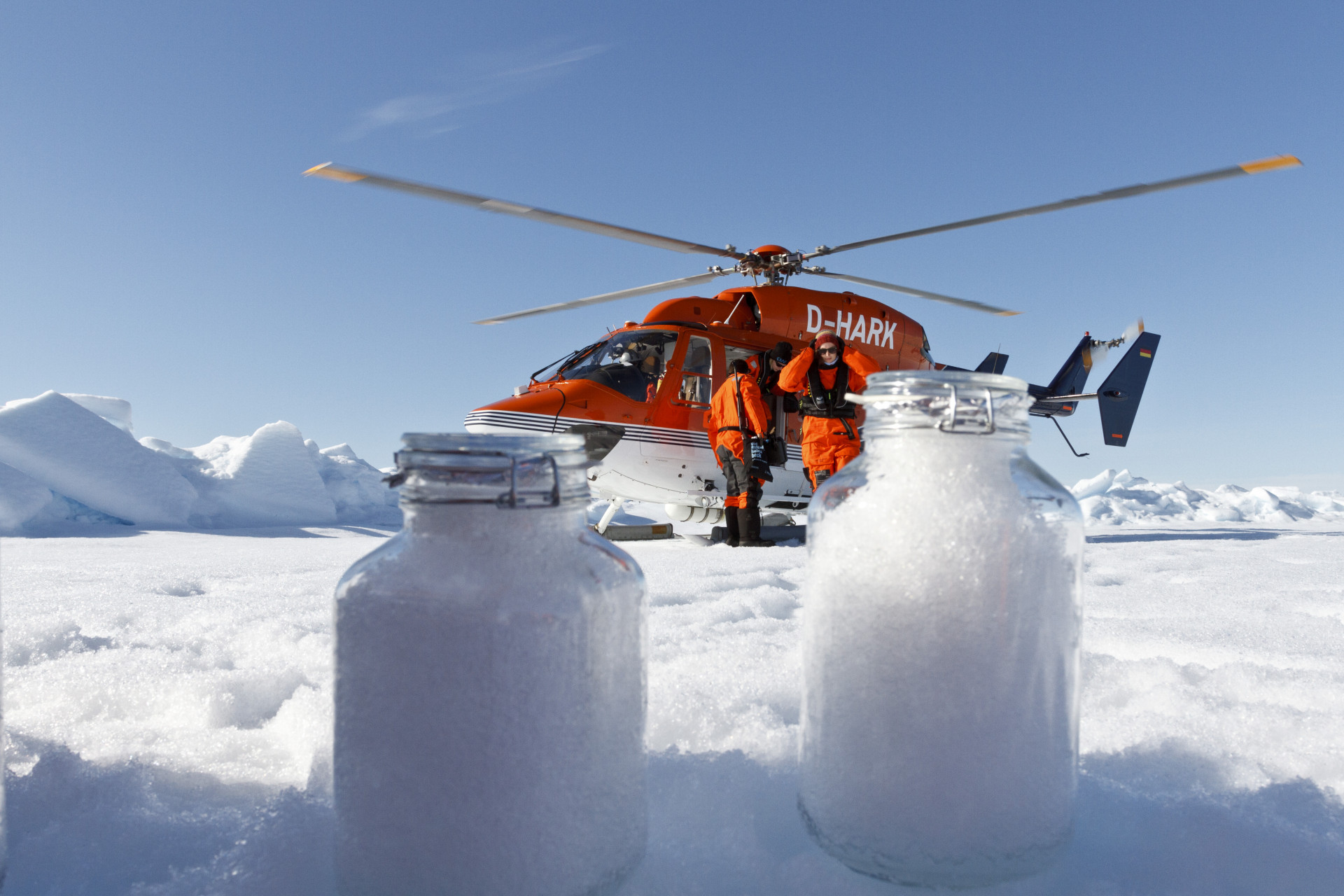 Einweckgläser mit Schneeproben vor rotem Hubschrauber in der Arktis