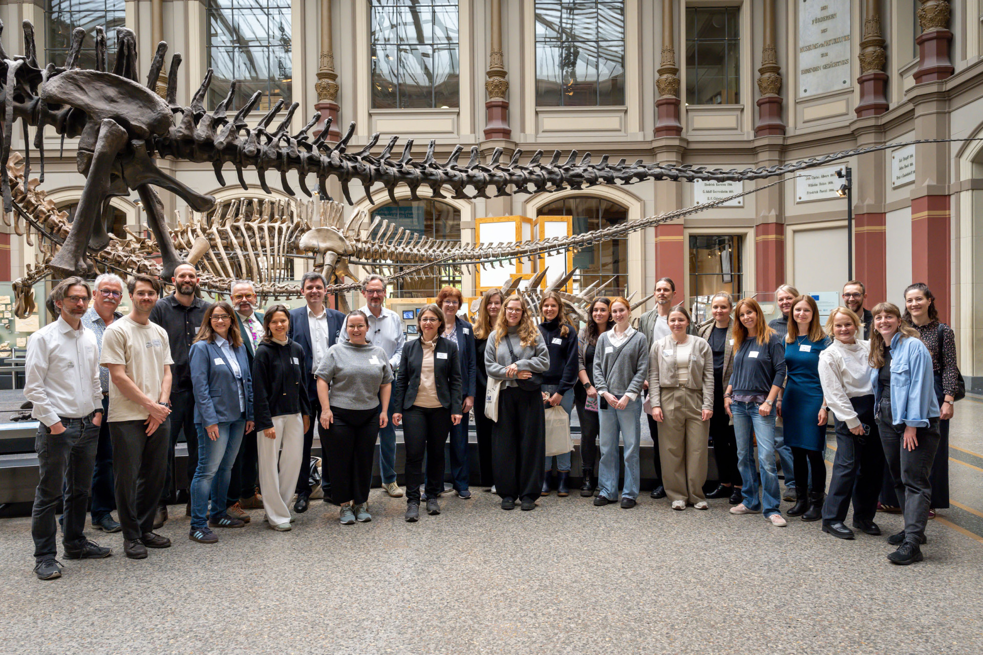 Eine Menschengruppe posiert vor einem Saurierskelett im Museum für Naturkunde Berlin