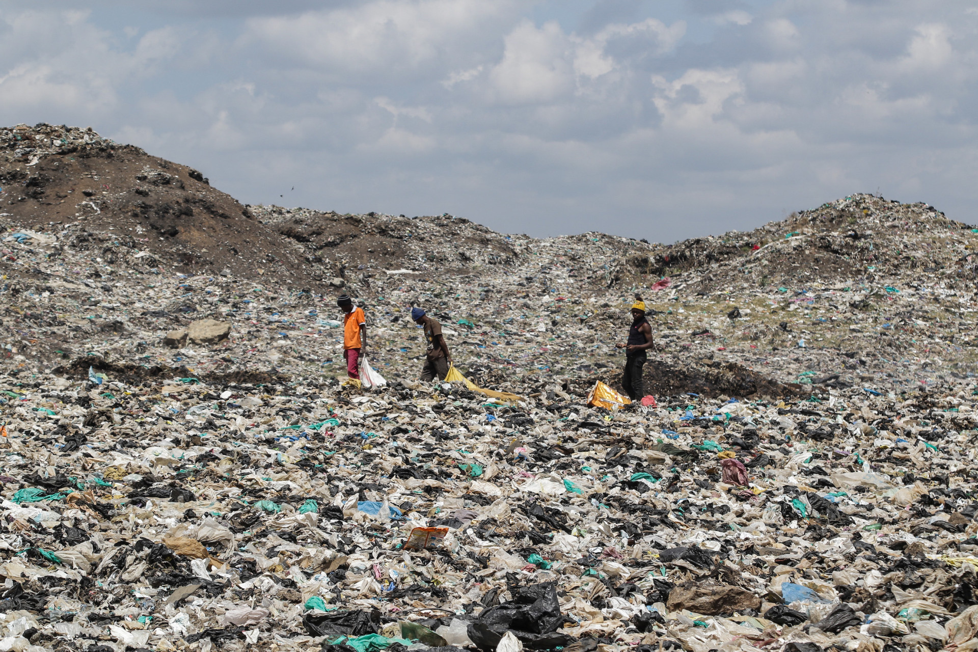 Drei Personen laufen über eine riesige Müllhalde mit Plastik und anderem Müll