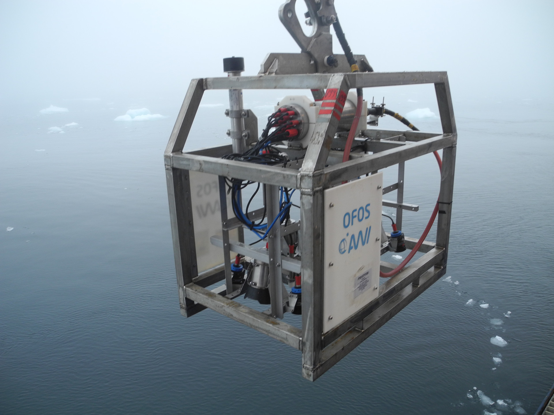 Wissenschaftliches Gerät in einem Metallkäfig schwebt über dem Wasser, auf dem kleine Eisschollen treiben