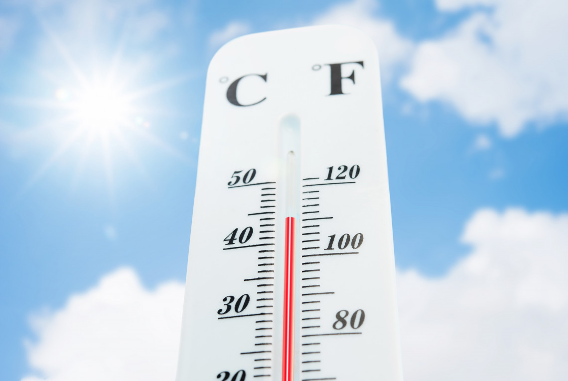 Ein Thermometer zeigt eine hohe Temperatur über 44 Grad an. Sonne und Himmel sind im Hintergrund zu sehen.