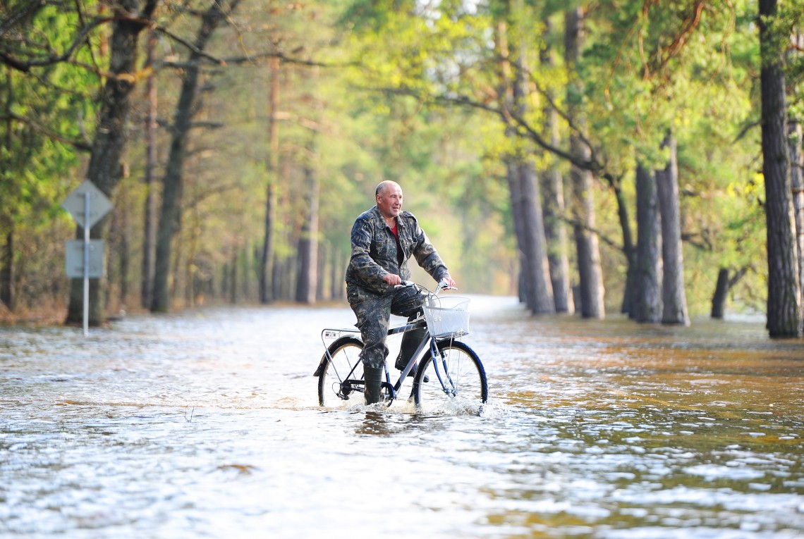 A man rides a bicycle along a flooded road.