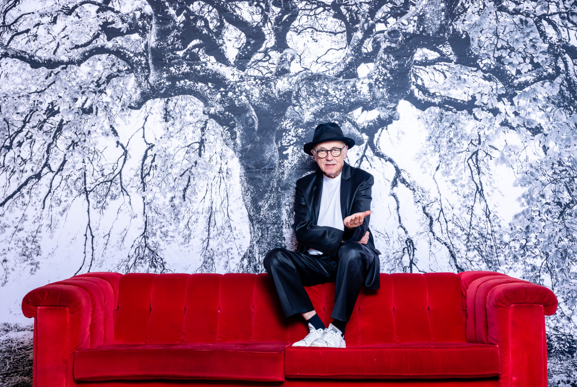 Horst Wackerbarth auf seinem roten Sofa vor dem Bild eines Baumes