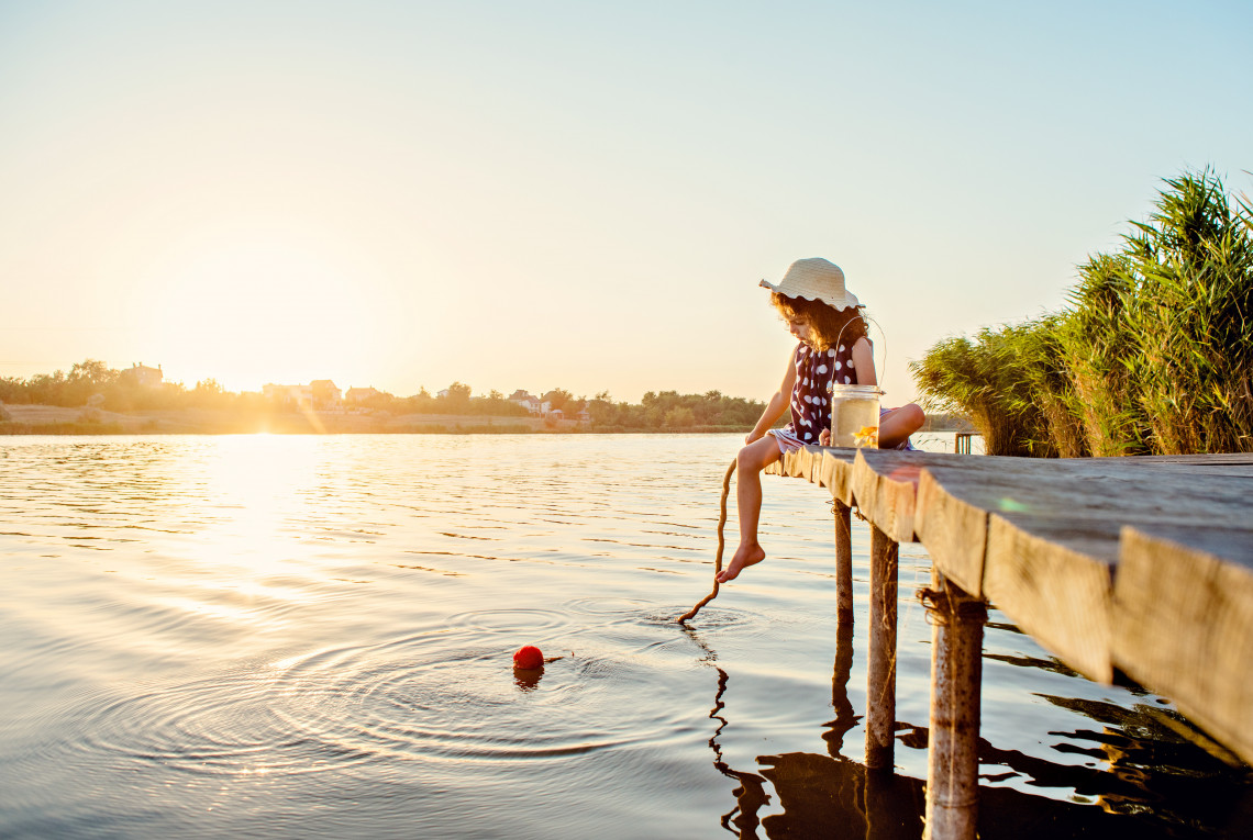 Sunset at the lake. A girl sits on a wooden jetty and is fishing.