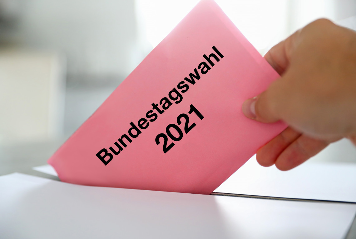 Hand wirft Umschlag mit Aufschrift "Bundestagswahl 2021" in Wahlurne