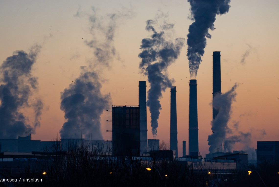 Fabrik im Sonenuntergang mit mehreren Türmen aus denen Rauch kommt.