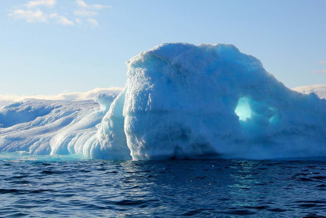 Ein blau-weißer Eisberg ragt an einer Eislandschaft aus dem Wasser