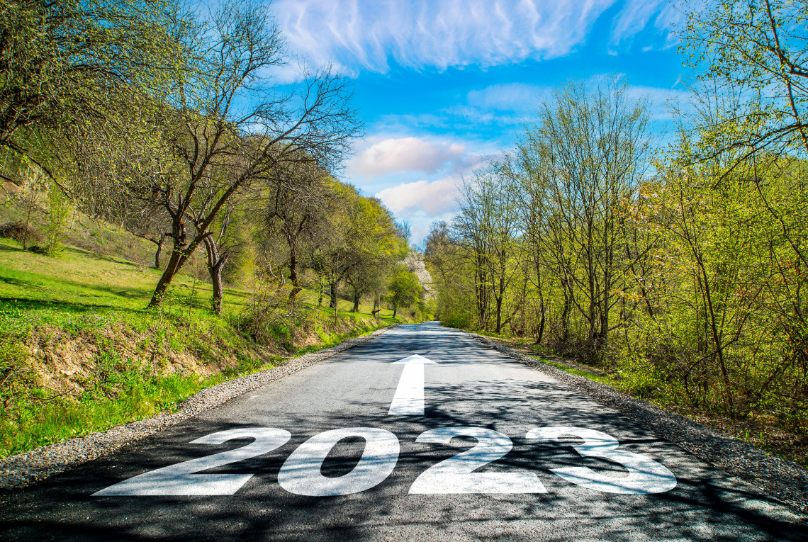 Eine Straße durch grüne Landschaft, auf der Fahrbahn steht groß "2023" - ein Pfeil zeigt darüber geradeaus die Straße hinauf.