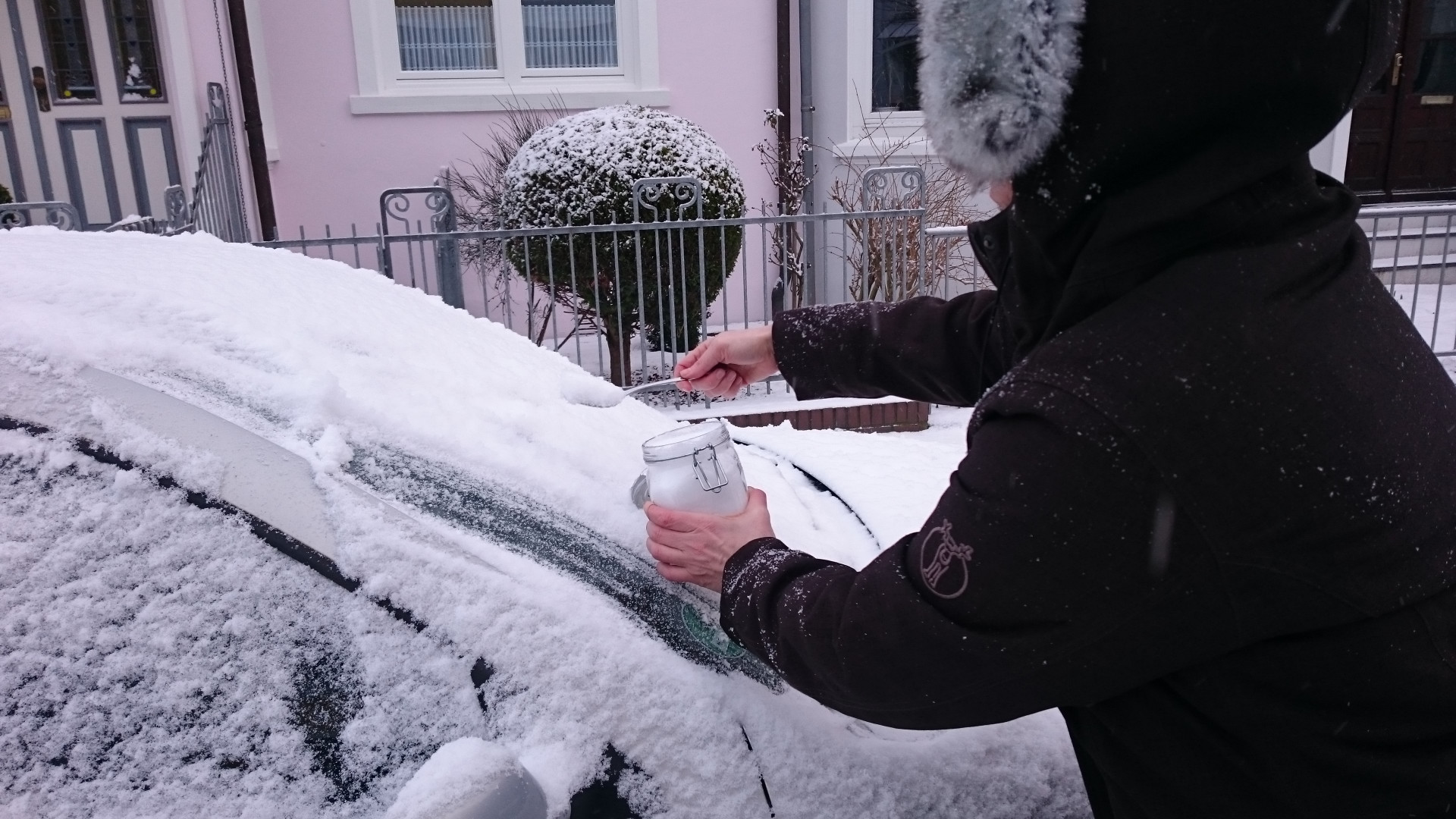 Wissenschaftlerin in Winterjacke sammelt Schneeprobe von einem Auto