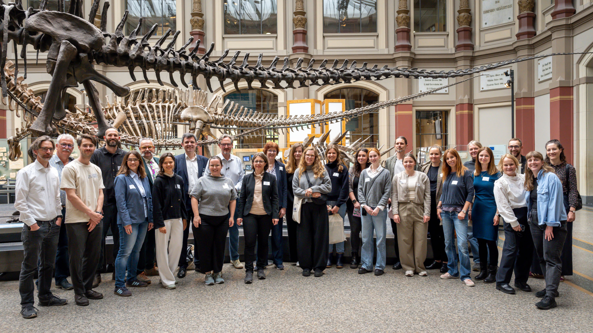 Eine Menschengruppe posiert vor einem Saurierskelett im Museum für Naturkunde Berlin