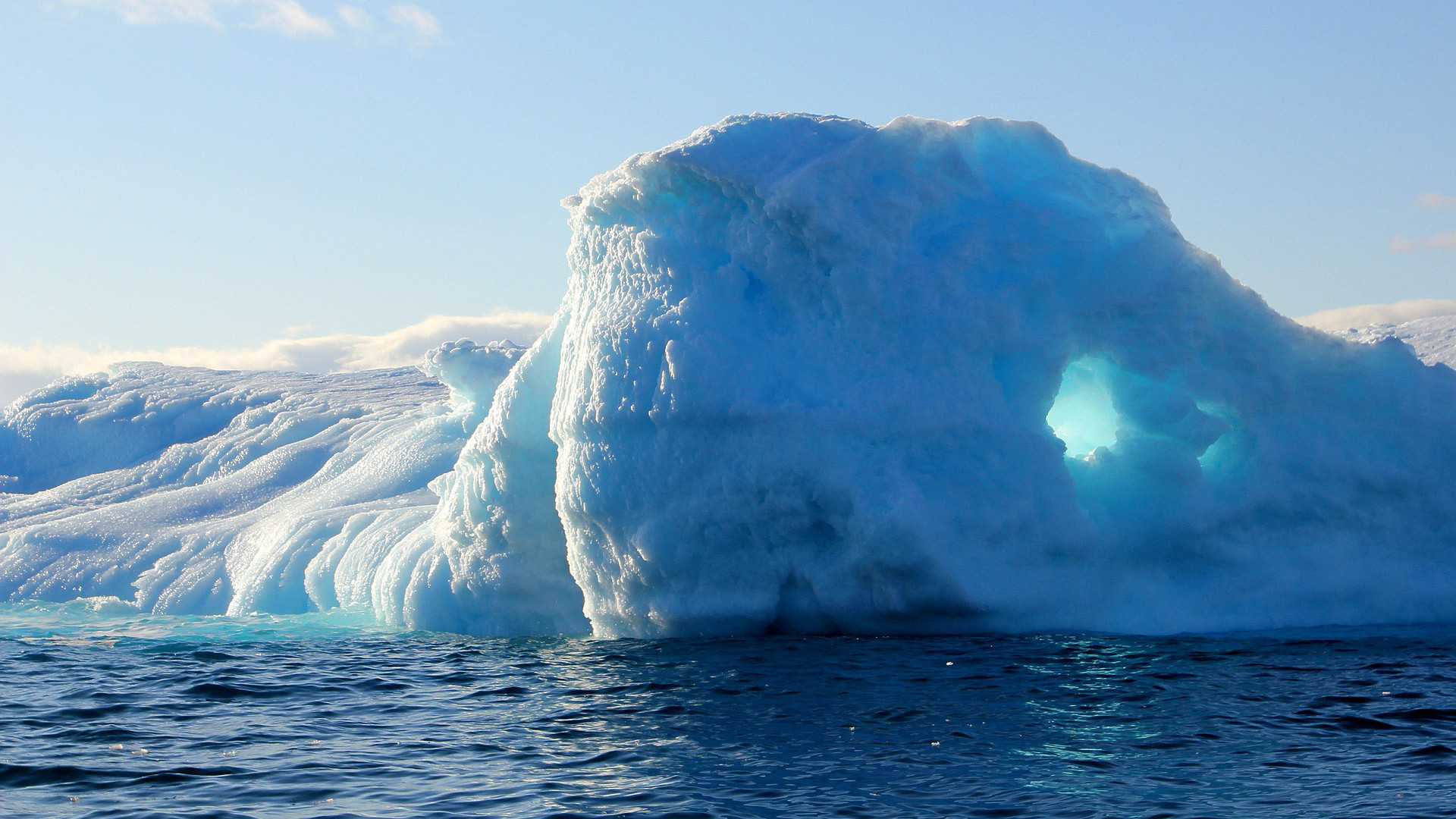 A blue and white iceberg rises out of the water at an icy landscape