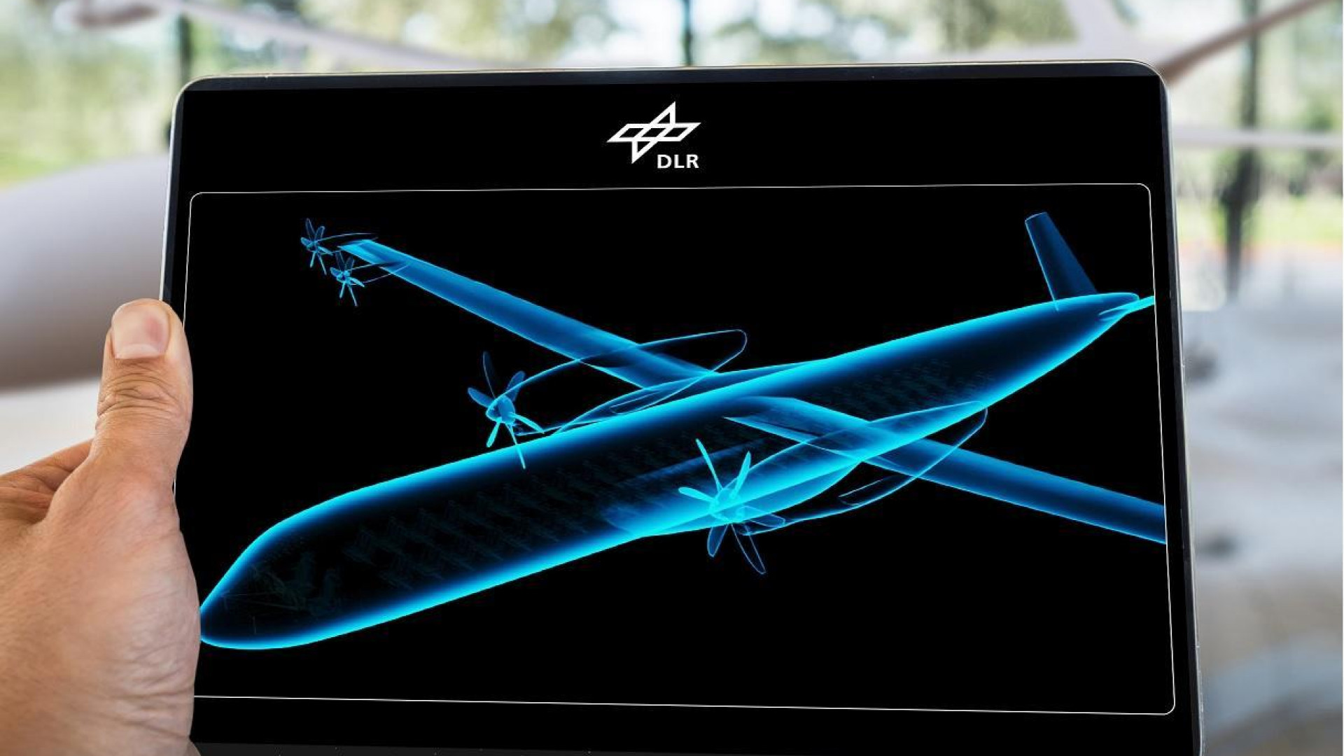 A futuristic blue aircraft silhouette on a tablet computer, held by a hand.